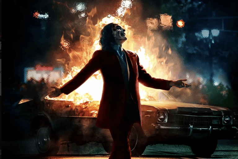 The Joker stands before a car that's on fire