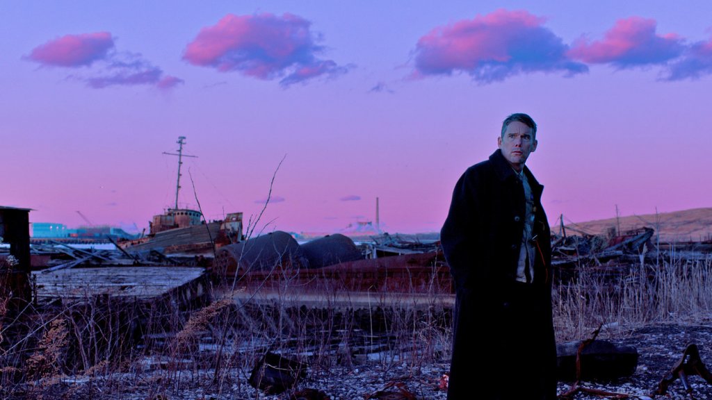 Reverend Ernst Toller (Ethan Hawke) stands in an abandoned shipyard with a pink sky in First Reformed (2017)
