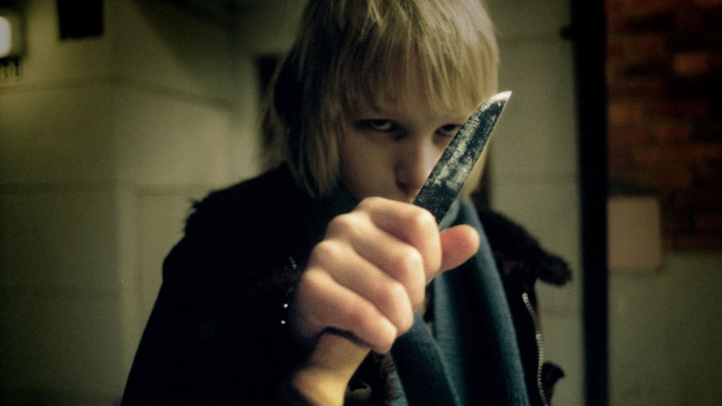 A young Swedish boy named Oskar (Kåre Hedebrant) holds a knife up to the camera in Let the Right One In (2008)