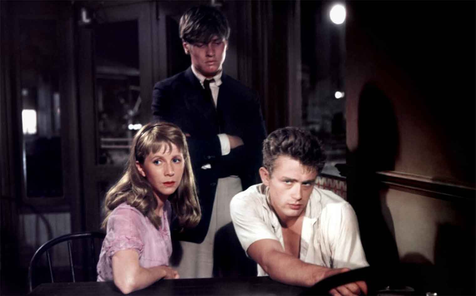Cal Trask (James Dean) and Abra Bacon (Julie Harris) sit at a table as Aron Trask (Richard Davalos) angrily looks over in East of Eden