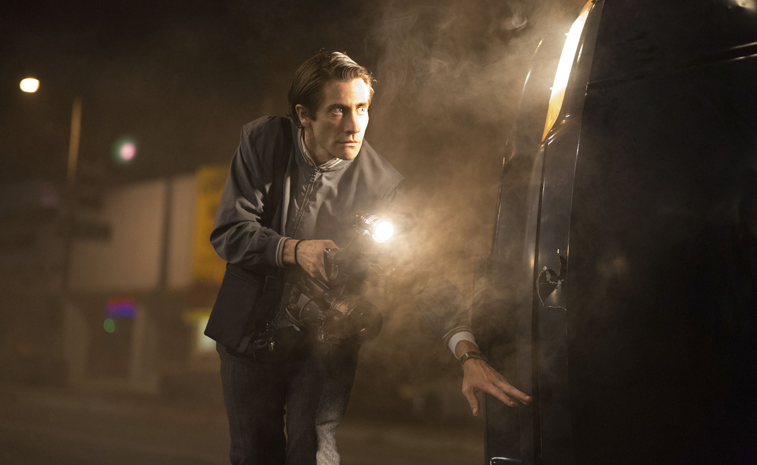 Lou Bloom (Jake Gyllenhaal) creeps around a car with a camera in Nightcrawler
