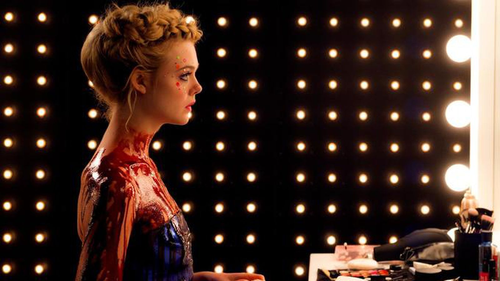 Jesse (Elle Fanning) looks into the mirror with lights surrounding her in The Neon Demon