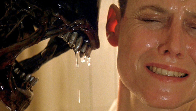 A Xenomorph shows its teeth inches away from Ripley's (Sigourney Weaver) face in Alien 3