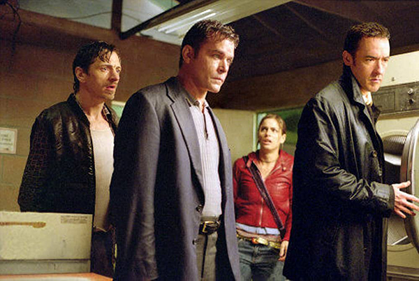 Three men in black coats and a woman in a red coat look at something offscreen in a laundry room