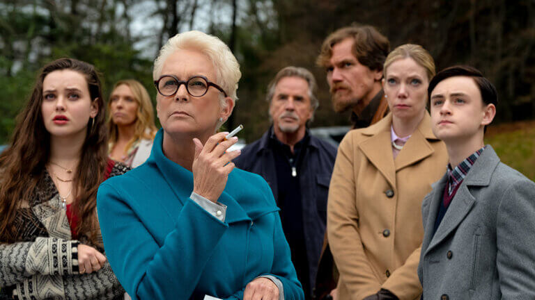 A woman in a blue coat holds a cigarette as several people stand around her looking offscreen