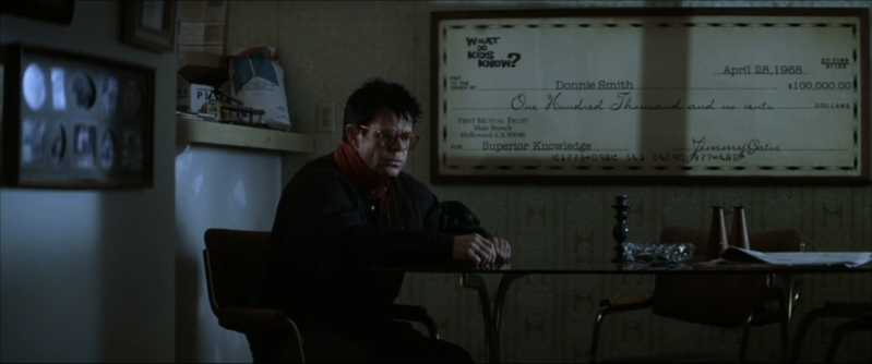 Donnie sits at his table with a giant check hanging in the background