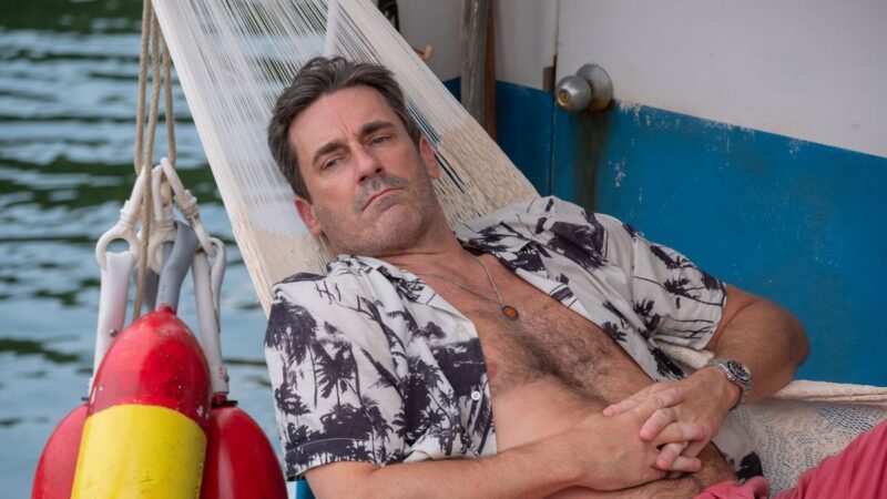 A man with his shirt open lies on a hammock on a boat
