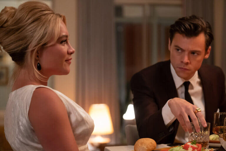 A man in a suit stares at his blonde wife in a white dress