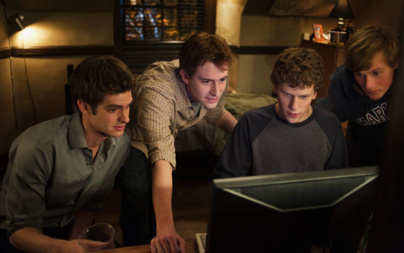Four boys gather around a computer in their dorm room in The Social Network