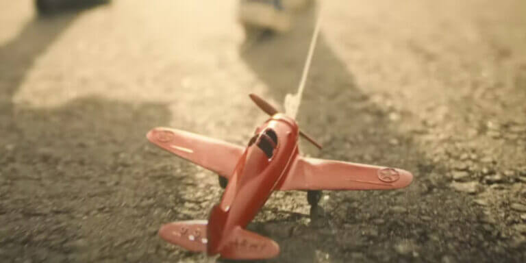 A boy pulls a small pink airplane along a road