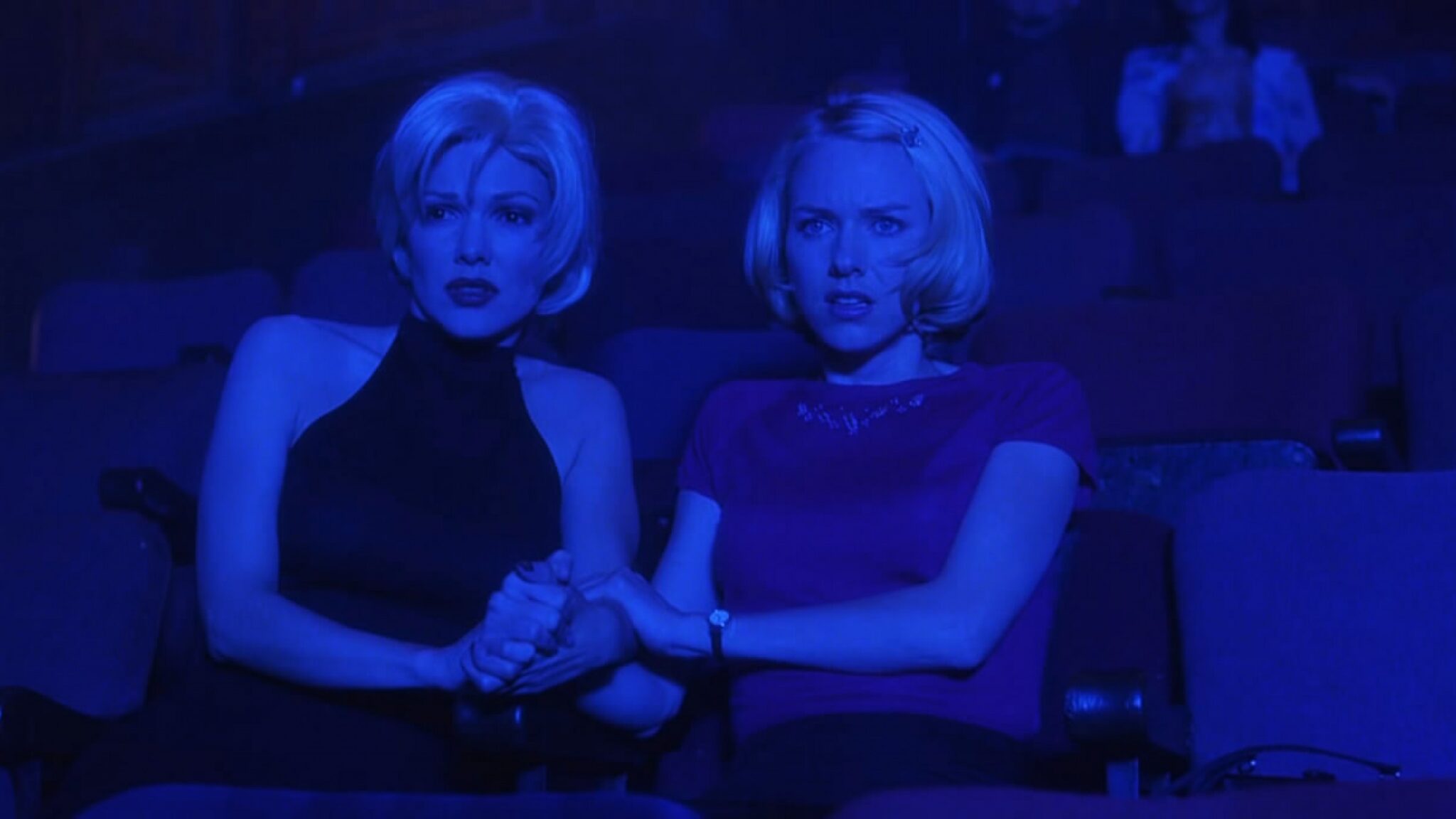Betty and Rita look scared in a theater lit by blue light