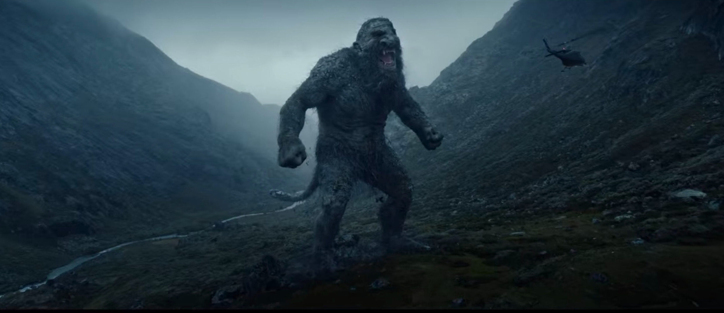 A giant troll stands in the hills between two mountains.