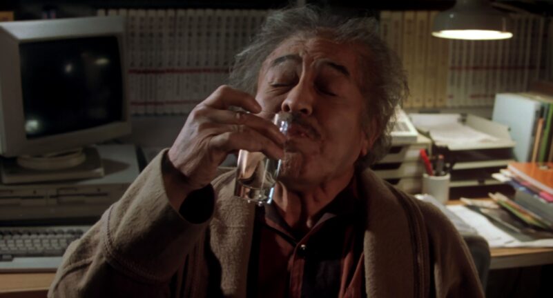 An elderly man drinks a small shot of alcohol mixed with water