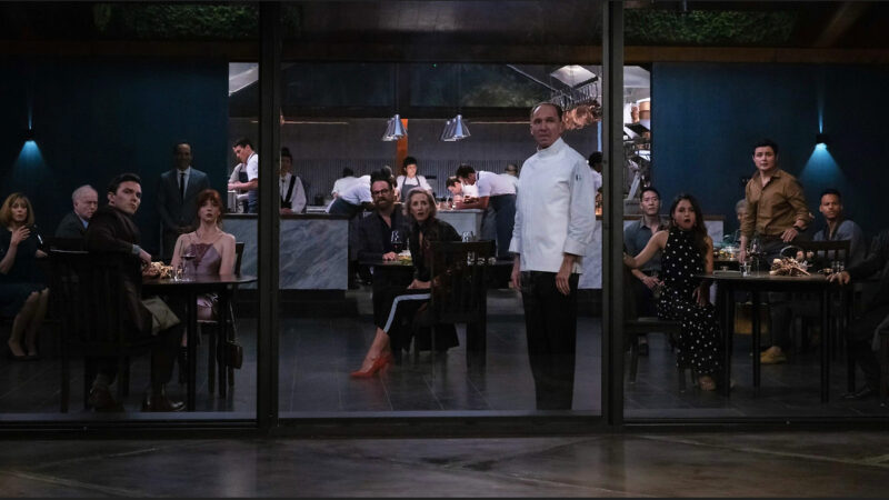 A chef stares out a window as his guests look on from behind