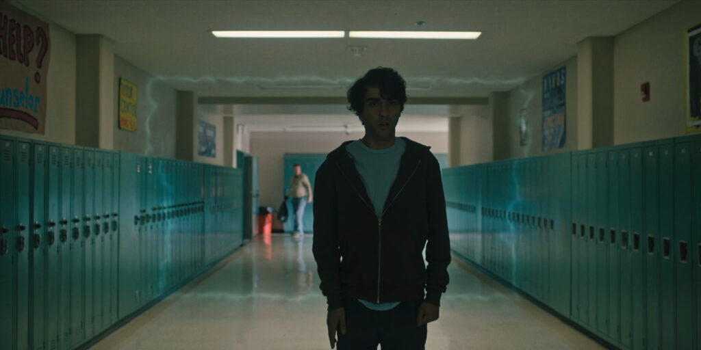 Peter Graham walks down the empty hallway of his high school, lockers on either side. A rectangle of light flows along the hallway, toward him. 