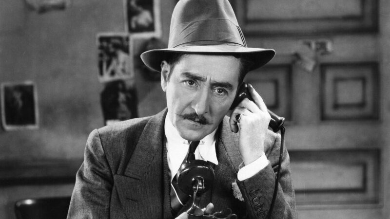 A man wearing a hat talks on an old telephone