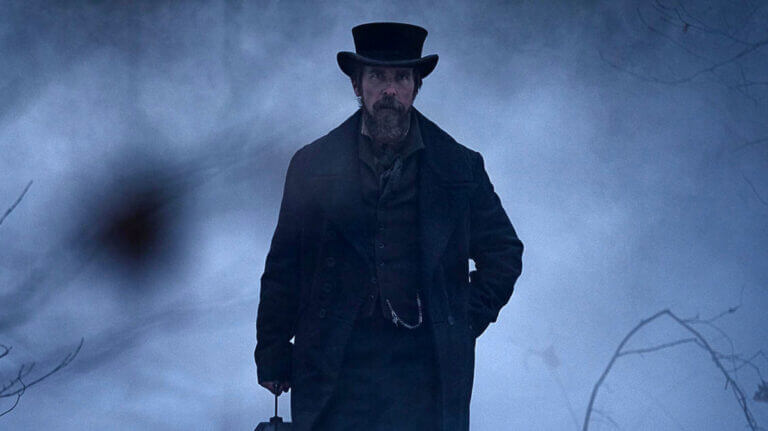 A man wearing a black coat and a black top hat walks in the snow