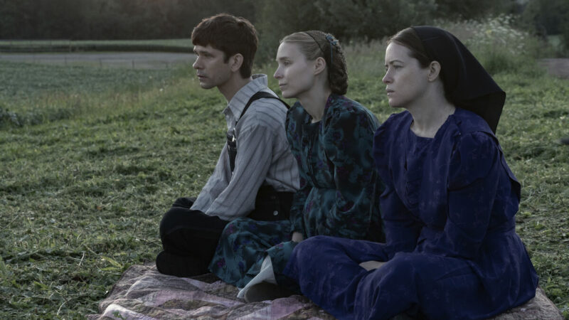 Two women and a man sit in the grass