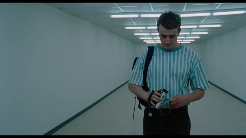 A man in a striped shirt puts his video camera away while looking down