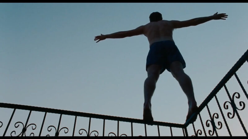 A man stands on the rail of a balcony