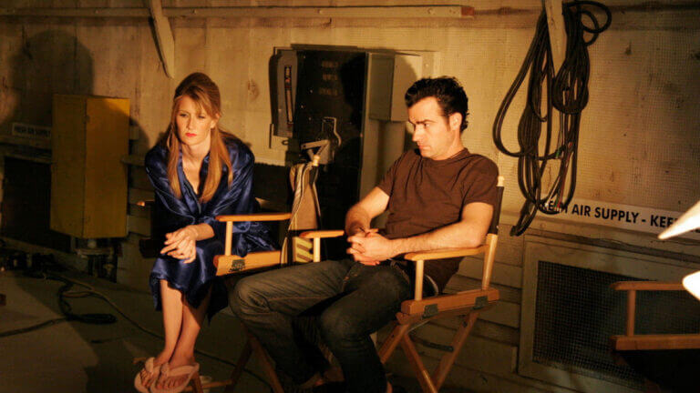 A woman and a man sit in actors chairs on a movie set