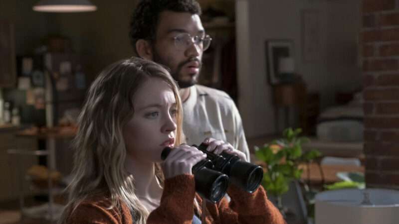 A woman holding binoculars and a man stare at something in shock