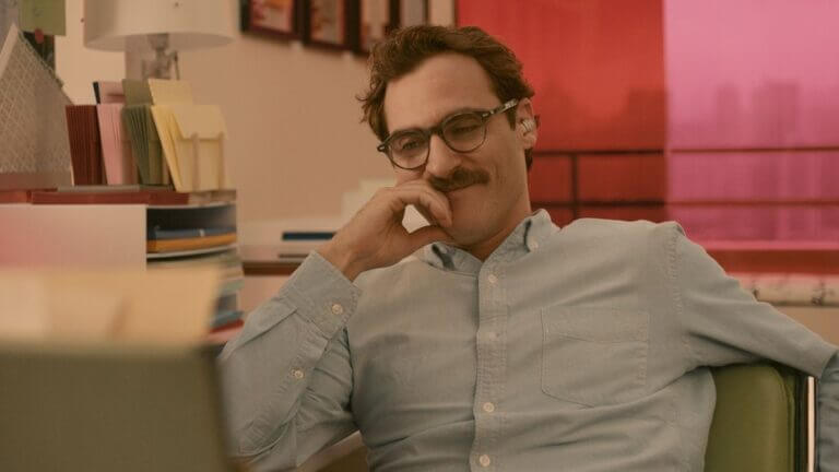 Theodore wears glasses as he sits in a chair and smiles