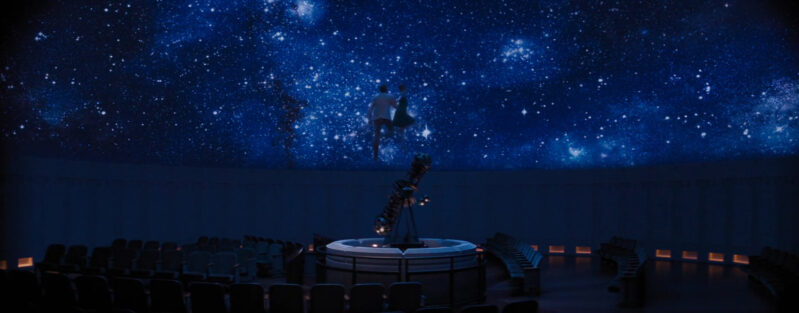 A man and a woman float into the starry sky of an observatory
