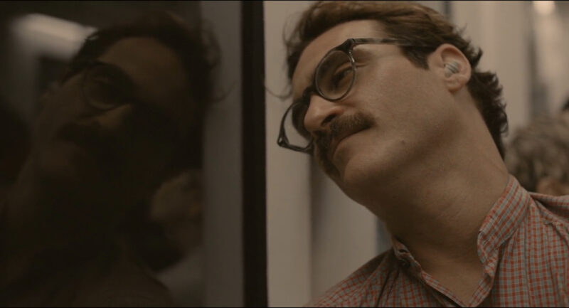 A man in glasses stares out a window, which bears his reflection