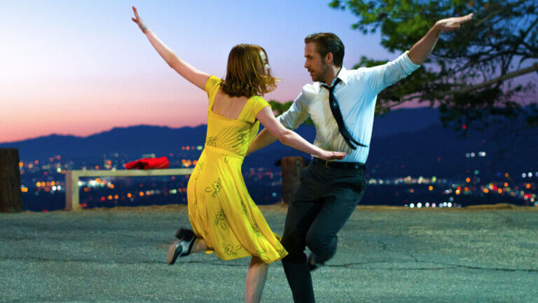 Mia, wearing a yellow dress, Sebastian, wearing a dress shirt and tie, dance outside