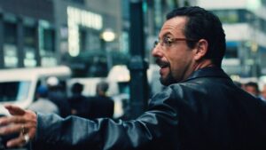 Howard, wearing a black leather jacket and glasses, points to something in a city