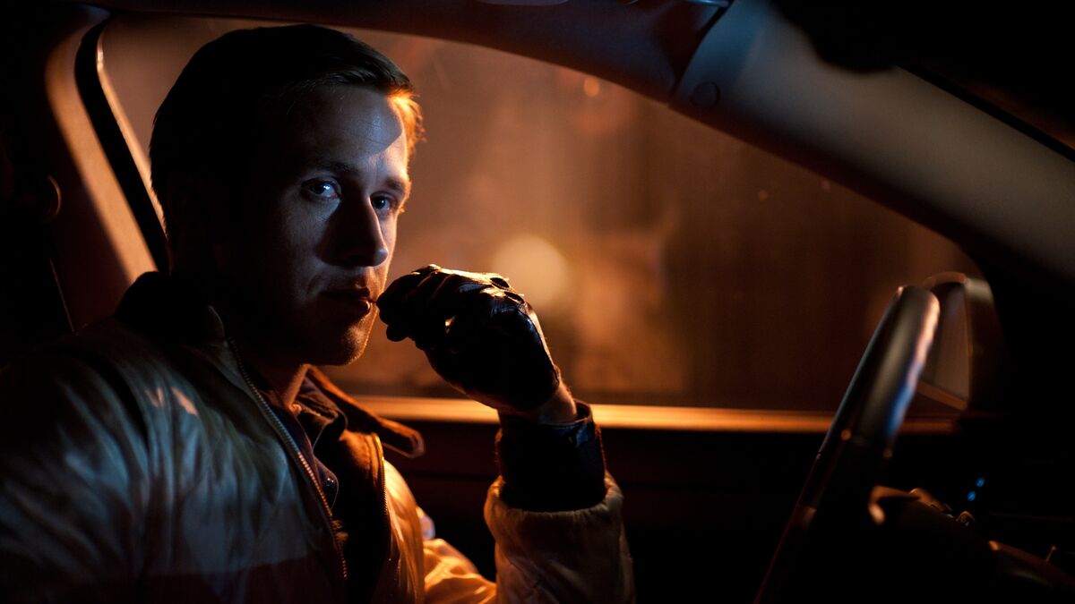 A man wearing leather gloves sits in a car chewing a toothpick at night