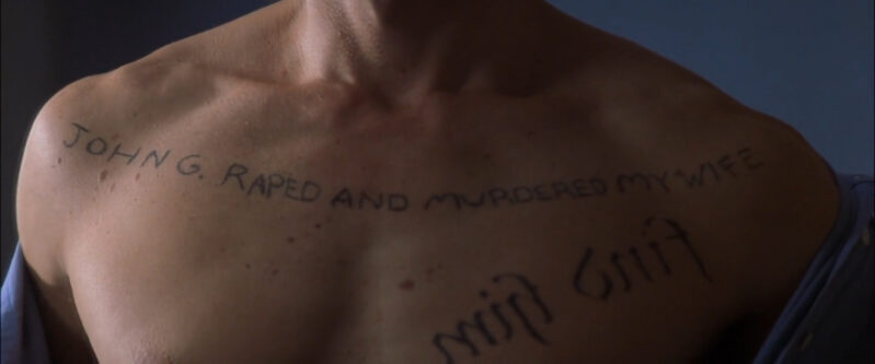 A man's bare chest has many words tattooed onto it