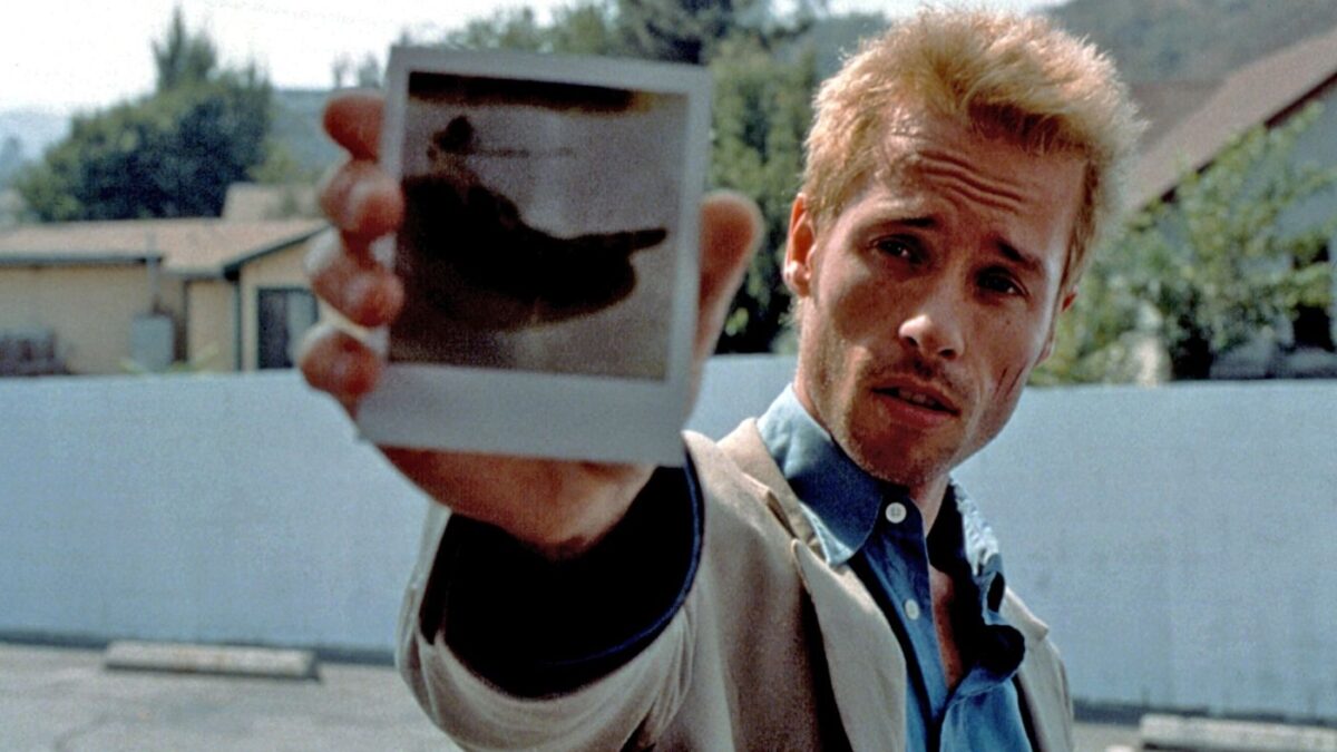 A blonde man holds up a polaroid picture