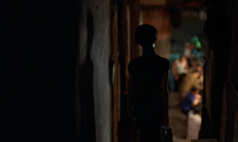 A woman shrouded in darkness walks in an alleyway