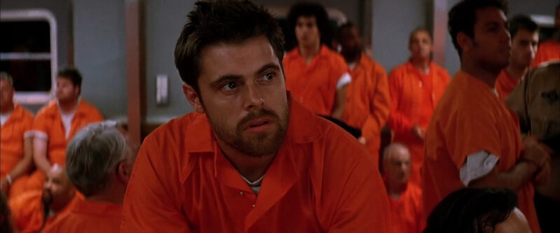 A man in a prison outfit is surrounded by other prisoners