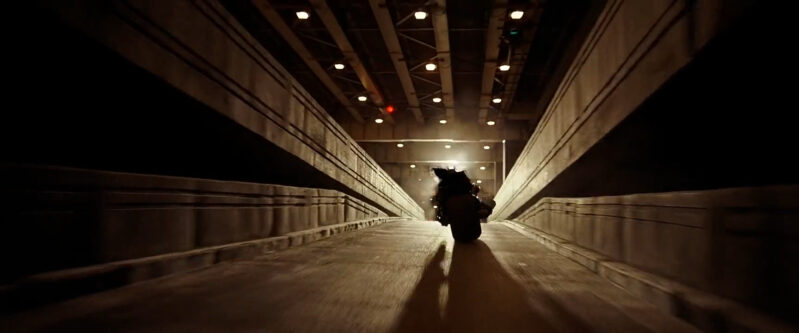 A man on a motorcycle exits a parking garage into the light