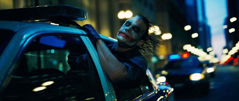 The Joker sticks his face outside a police car as it drives