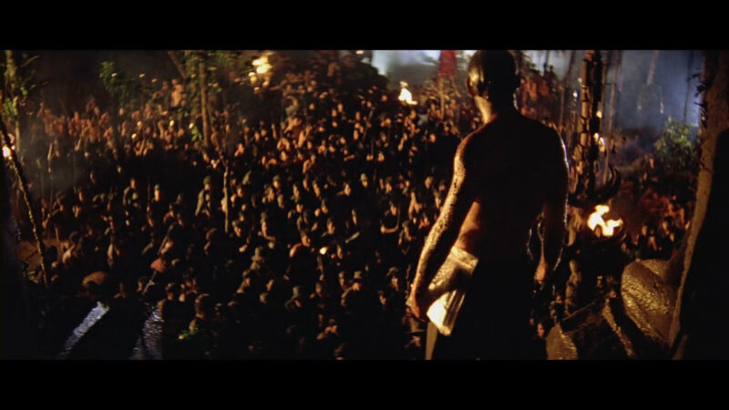 A man stands before a crowd of people in a jungle