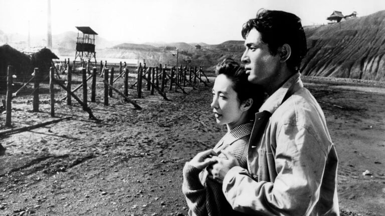 A man holds a woman as they look on in a POW camp