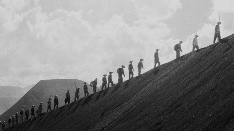 Several Chinese prisoners walk up a desert hill