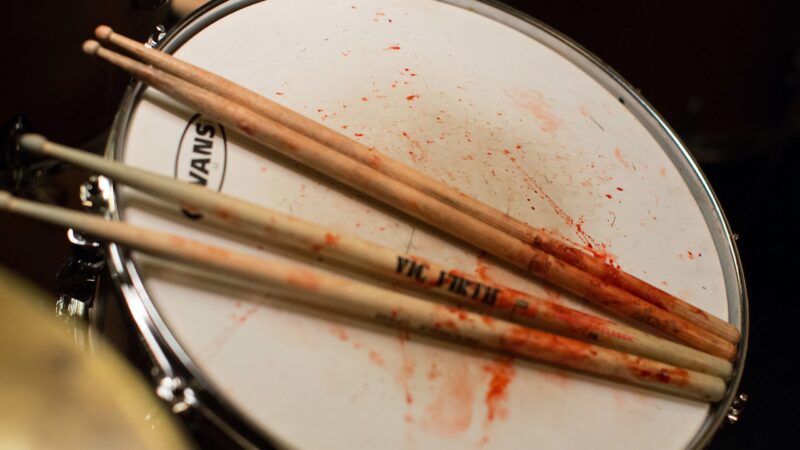 Four bloodied drumsticks sits atop a drum