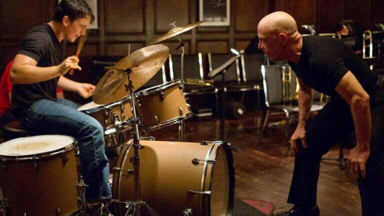 Andrew plays the drums while Fletcher crouches beside him
