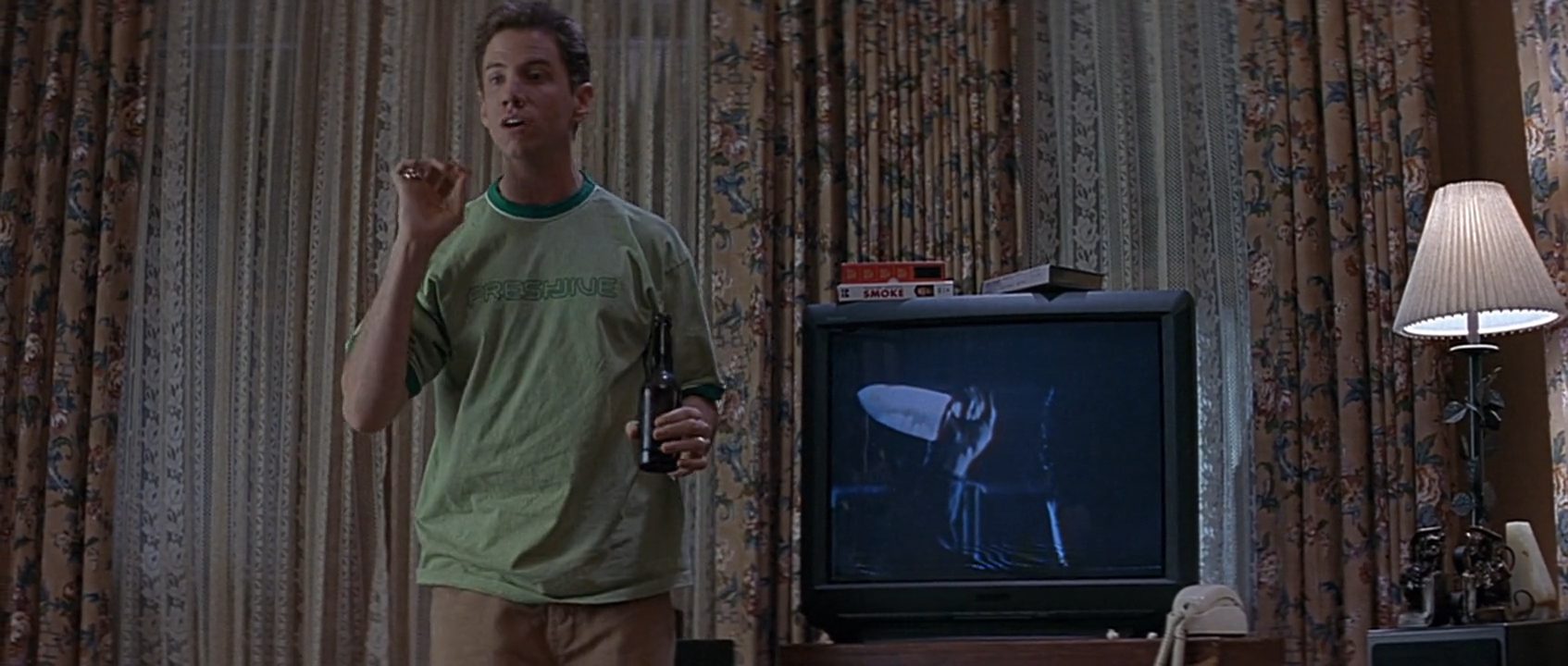 Randy stands in front of the television, which is playing the movie Halloween, as he explains the rules of horror movies