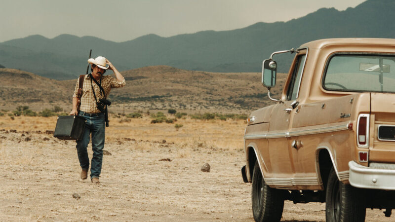 Llewelyn Moss walks across a desert with a gun and a briefcase towards his car