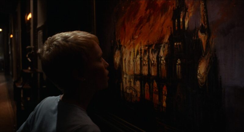 Rosemary looks at a painting of a church and multiple crosses on fire