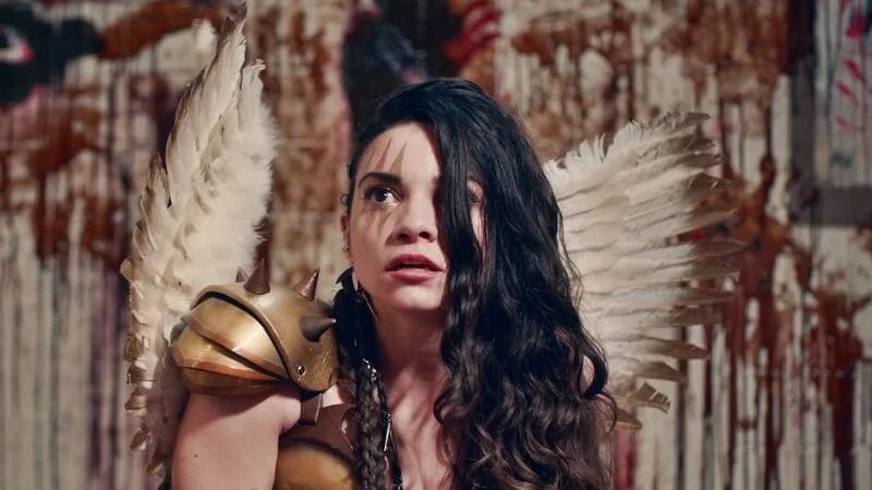 Sienna wears angel wings and a Valkyrie costume in a bloodied room