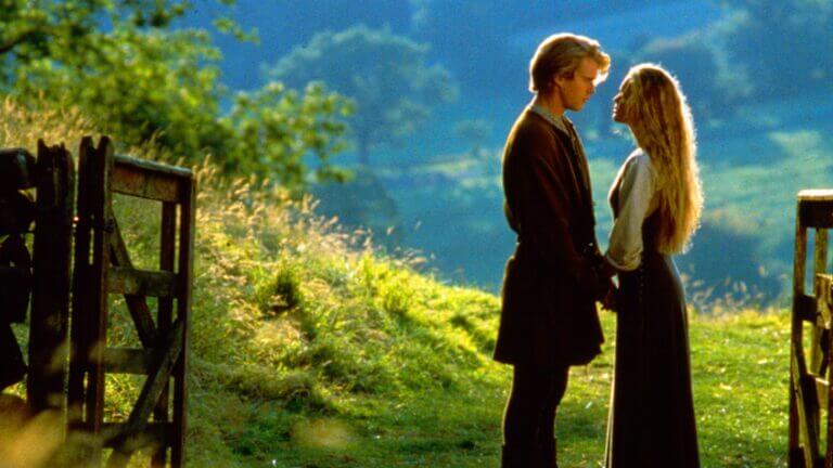 Westley and Buttercup hold each other's hands in a field