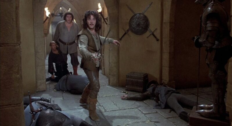Inigo Montoya raises his sword to fight Count Tyrone Rugen while Westley and Fezzik stand in the background