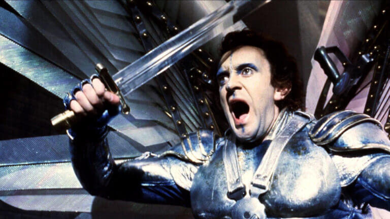 A man in armor, holding a swords, lets out a battle cry